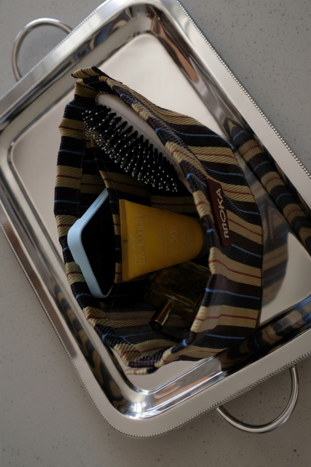 Pochette MOKA Cabanon rayée en matériaux recyclés, artisanale, contenant des accessoires de beauté sur un plateau