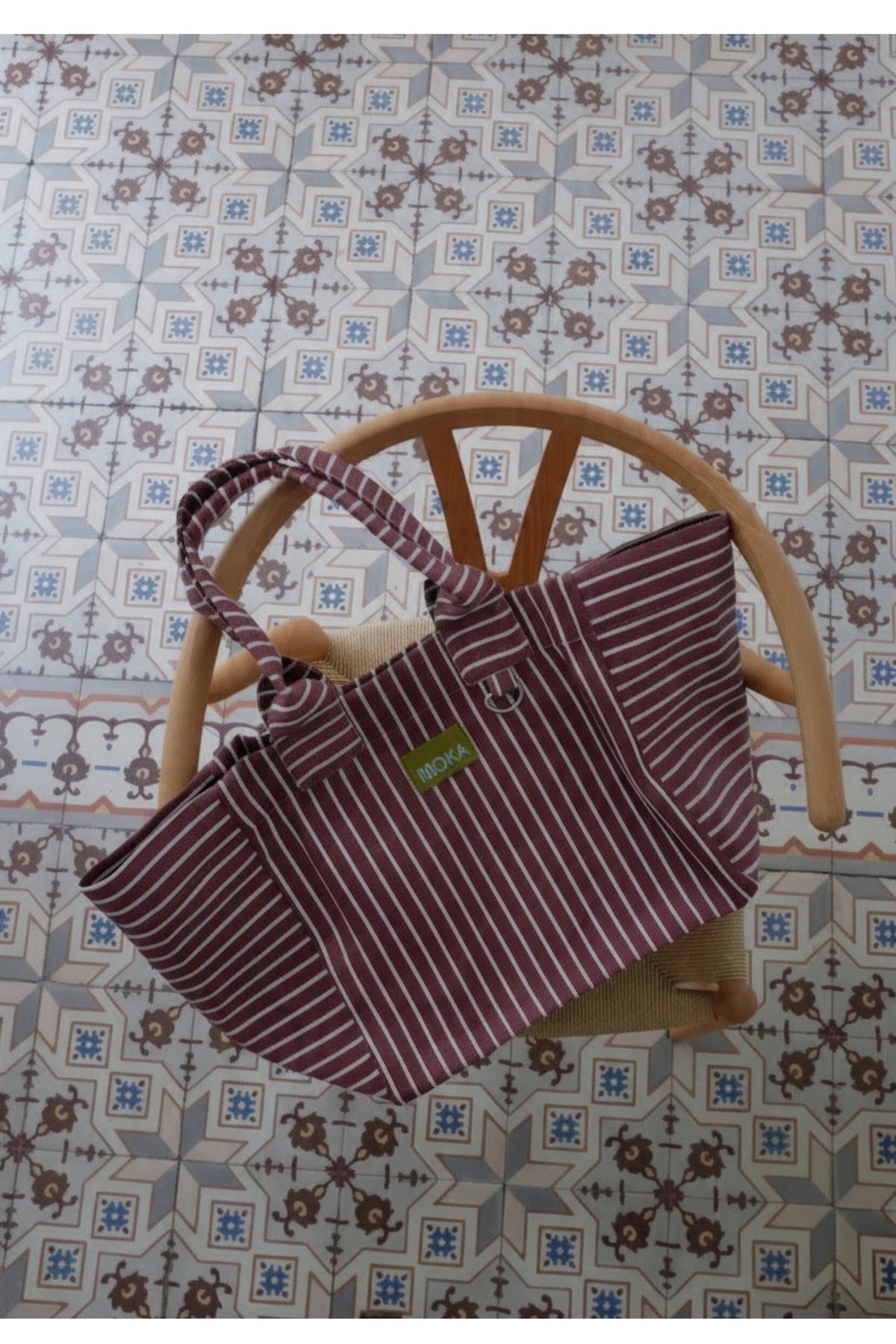 Grand sac MOKA rayé bordeaux et blanc en matériaux recyclés posé sur une chaise en bois