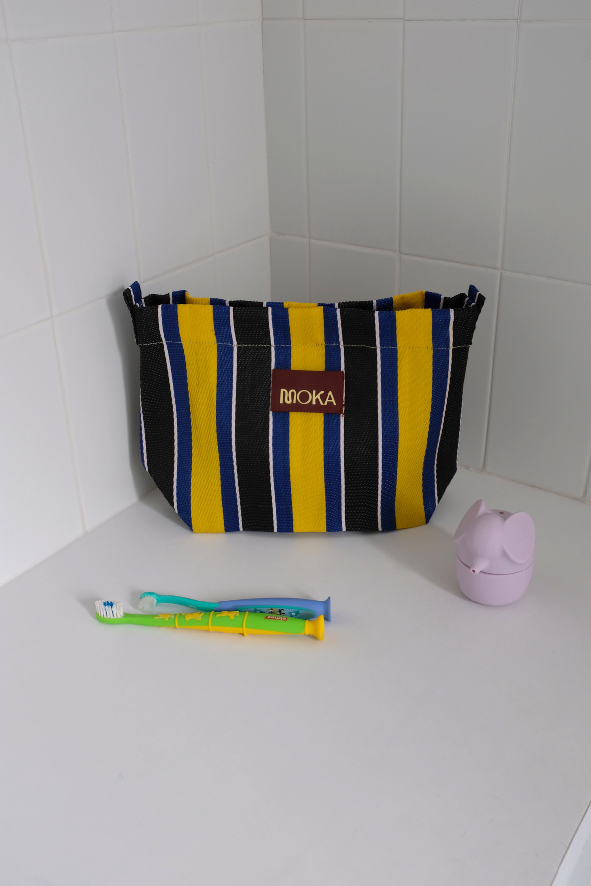 Pochette MOKA rayée bleu, jaune et noir fabriquée à la main en matériaux recyclés posée sur un rebord de baignoire