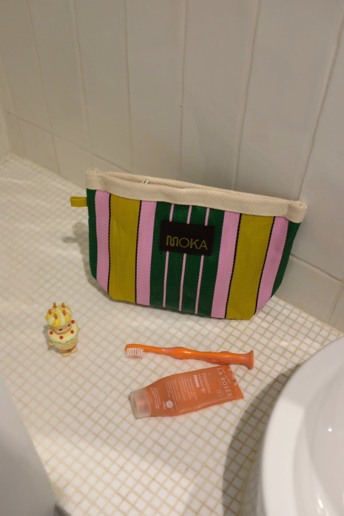 Petite pochette MOKA Lollipop à rayures verticales roses, vertes et jaunes en matériaux recyclés sur un lavabo