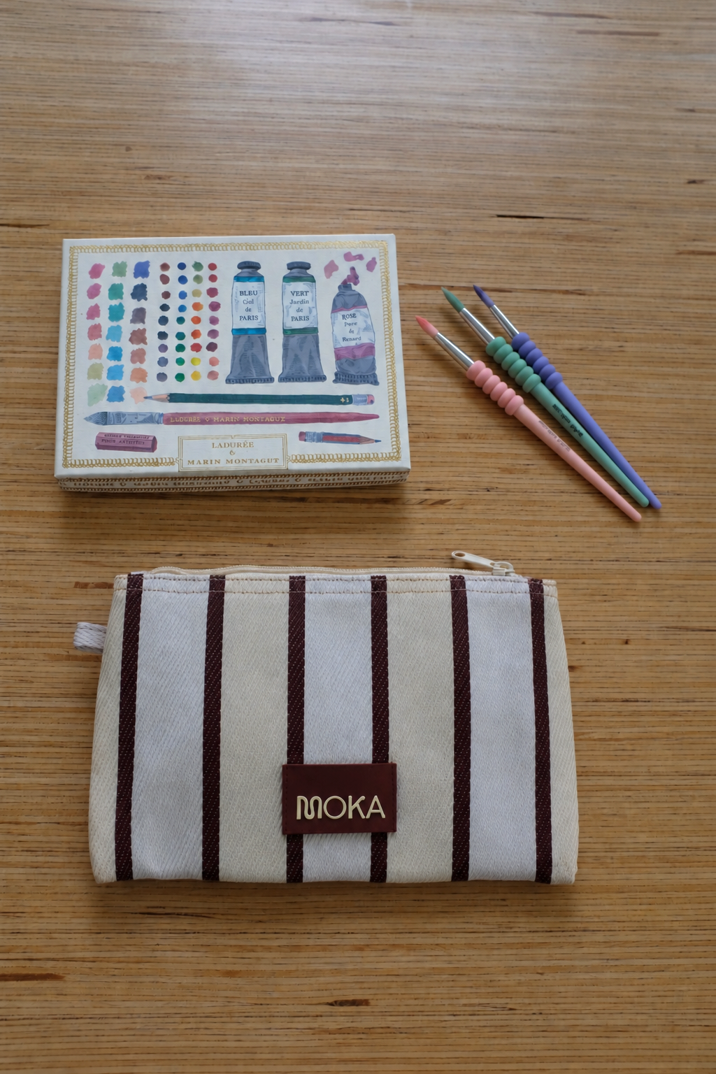 Trousse MOKA modèle Coconut en toile rayée beige et marron avec étiquette logo, posée sur une table en bois