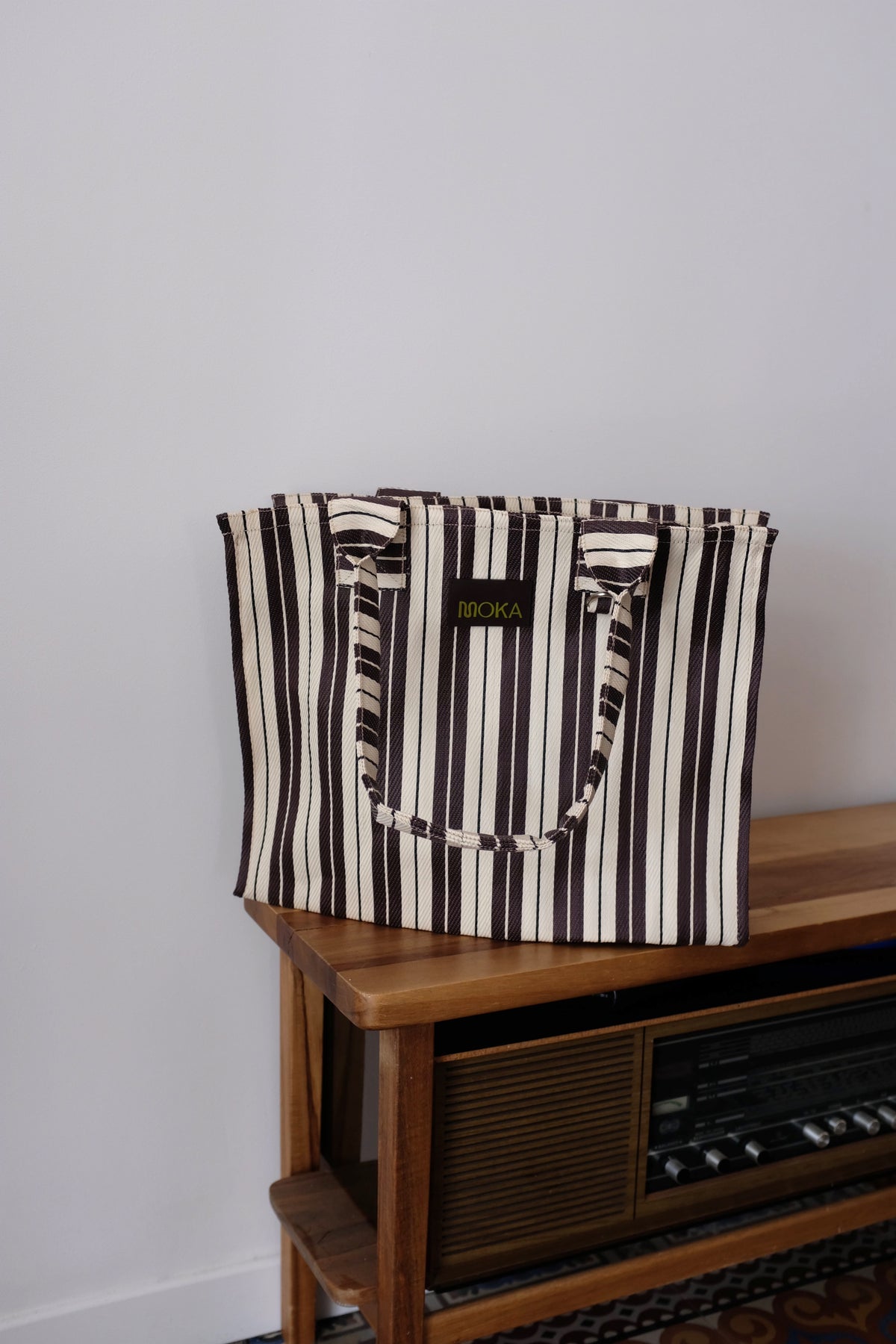 Sac du marché MOKA rayé marron et blanc en matériaux recyclés avec étiquette de marque sur meuble en bois
