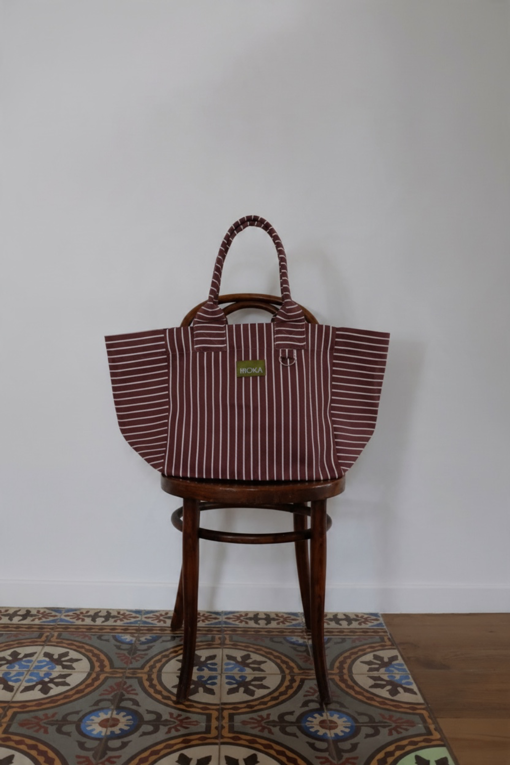 Grand sac MOKA Merlot à rayures blanches, fabriqué à la main en matériaux recyclés, posé sur une chaise en bois.